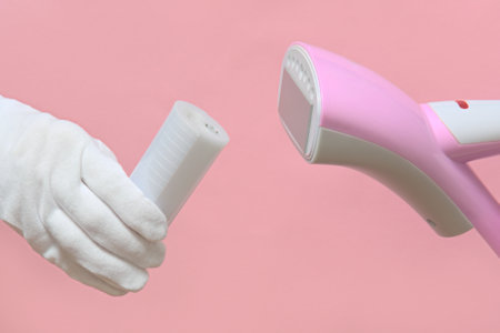Man of the gloves holding a disassembled clothes steamer with a plastic water container. pink background.の写真素材