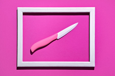 Ceramic knife with a pink handle in a white photo frame. Magenta background. conceptの写真素材