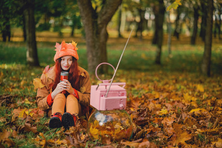 Red-haired young hipster woman watching retro TV in the park in the fall. recreation concept.の写真素材