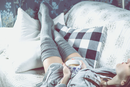 Young girl is drinking tea on the sofa, cozy conceptの写真素材