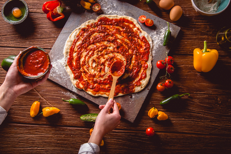 Girl is placing tomato sauce on fresh pizzaの写真素材