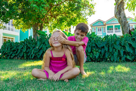 A smiling boy closing eyes to a little girl sitting on green grass in a summer gardenの写真素材
