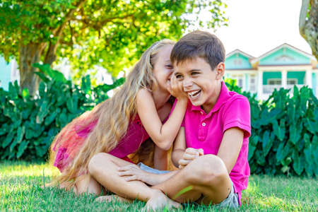 Little girl whispering a joke in a boy's ear, the boy is laughing, summer garden background