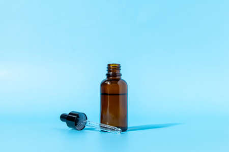 Cosmetic bottle with a brown glass dropper on a blue background casts a shadow. Front view with copy space. Mockup of a cosmetic product. Serum for skin care.の写真素材