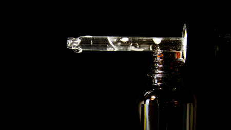 Dropper bottle for cosmetic product isolated on black background. Serum for skin care. Creative presentation, front view with copy space. Mockup of a cosmetic product.の写真素材