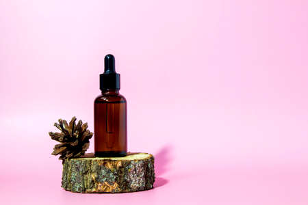 Brown glass serum bottle with pipette and pine cone on pink background with copy space. Body care serum cosmetic skin care. Front view with copy space. Mockup of a cosmetic product.の写真素材