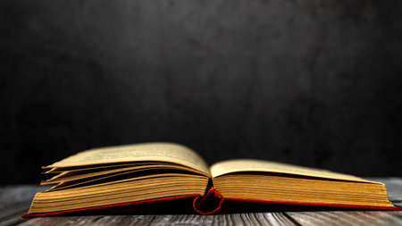 Image of an open antique book on a wooden table with old yellow sheets and dust on a dark...