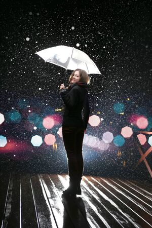 Beautiful woman with white umbrella in flash lights and rain dropsの写真素材
