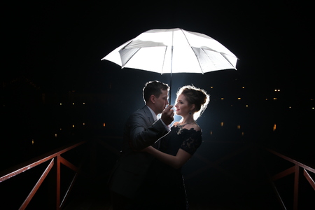 Beautiful couple man with woman with white umbrella in flash lights and rain dropsの写真素材