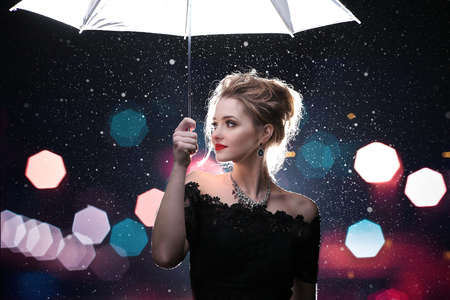 Beautiful woman with white umbrella in flash lights and rain dropsの写真素材
