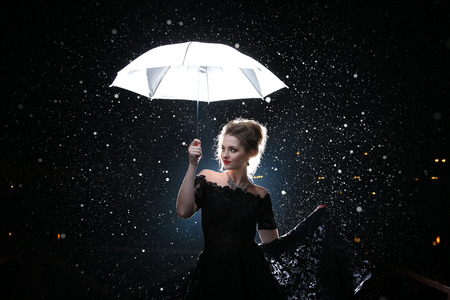 Beautiful woman with white umbrella in flash lights and rain dropsの写真素材