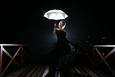 Beautiful woman with white umbrella in flash lights and rain dropsの写真素材