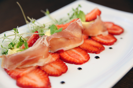 layered dessert with strawberries, biscuit cake and cream cheese on a dark wood backgroundの写真素材