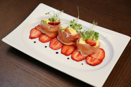 layered dessert with strawberries, biscuit cake and cream cheese on a dark wood backgroundの写真素材