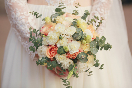beautiful bouquet of different colors in the hands of the bride in a white dressの写真素材