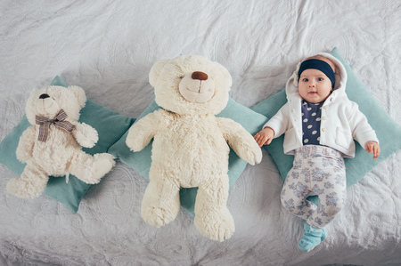 Adorable two month old baby girl lying on the pillow with two bearsの写真素材