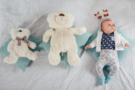 Adorable two month old baby girl lying on the pillow with two bearsの写真素材