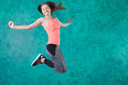 Sport young female in fashion sportswear jumping over turquoise background.の写真素材