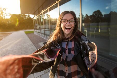 Young smiling female student near modern architecture in autumn sunset