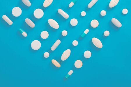 Assorted pharmaceutical medicine pills, tablets and capsules over blue background
