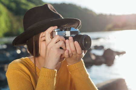Young woman traveler is taking pictures of nature on retro cameraの写真素材