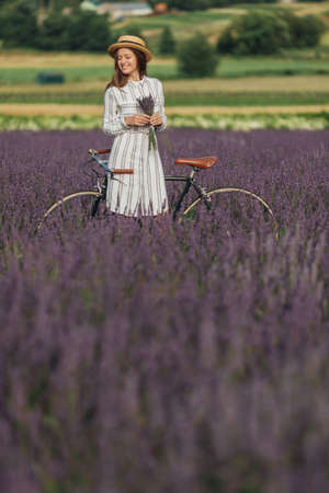 Young woman with retro bicycle and lavender bouquet on violet flowers field backgroundの写真素材