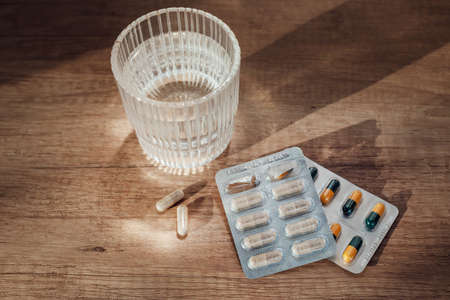 Pills capsules medicine and glass of water on wooden background