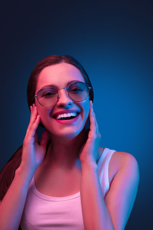 Neon close up portrait of young woman round sunglasses and white dress on dark blue backgroundの写真素材