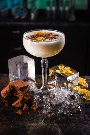 White cocktail drink with milk chocolate, corn flakes, ice cubes on black backgroundの写真素材