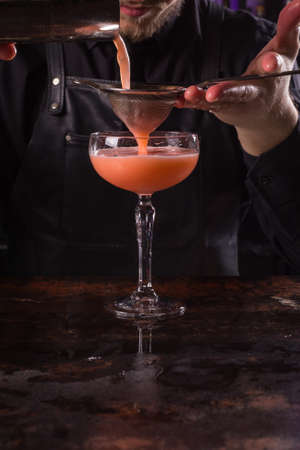 Bartender dressed in black apron and shirt make cocktail drink on black backgroundの写真素材
