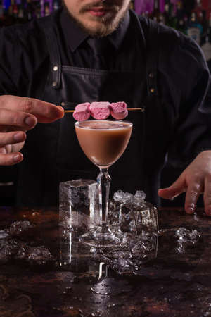 Bartender dressed in black apron and shirt is decorating cocktail drink on black backgroundの写真素材