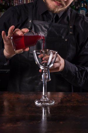 Bartender dressed in black apron and shirt make red cocktail drink on black backgroundの写真素材