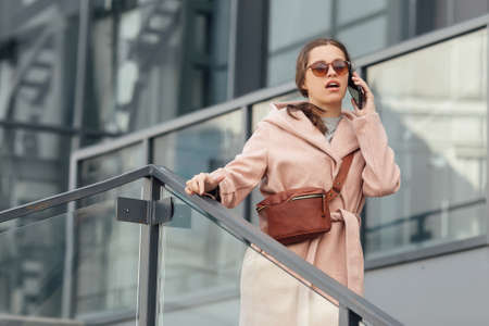 Woman in pink dress talking to smarthone outdoor on grey urban city backgroundの写真素材