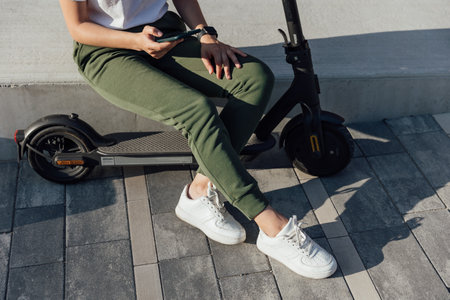 Young woman in white sneakers is sitting on electric scooterの写真素材