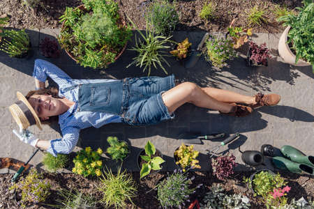 A female gardener in a straw hat lies near many perennials and garden tools