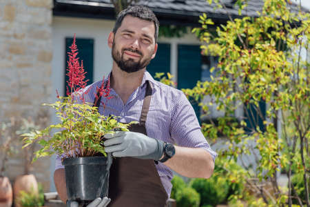 Young man gardener with perennial plant in hands in garden center