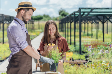 Young woman and man-gardener take care perennial plant in garden centerの写真素材