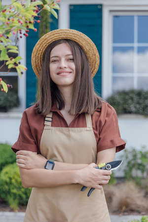 Young woman-gardener with garden scissors in hand standing in front of garden house