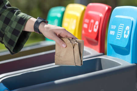 Woman throws trash in sorting color wastebasket in park outdoor