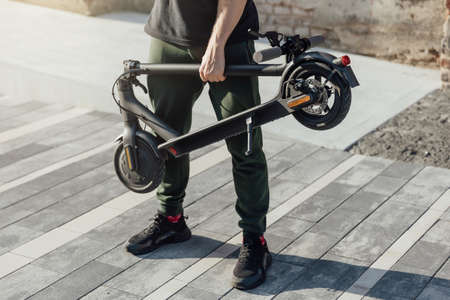 Man hold folded electric scooter in hands for transportation into work officeの写真素材