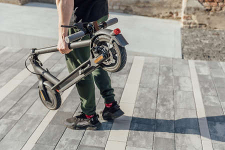 Man hold folded electric scooter in hands for transportation into work officeの写真素材