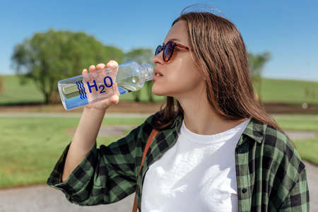 Young woman drinks water from reusable bottle outdoors. Refreshing drink