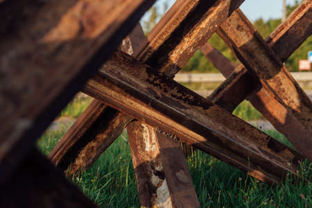 Rusty anti-tank hedgehogs on the wet grass on sunset background. War in Ukraineの写真素材