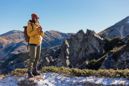 Portrait of a woman hiker standing with cup f tea on the slope of mountain ridge against mountainsの写真素材