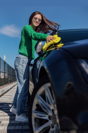 A young female cleaning and polishing her car hood with microfiber cloth. Concept of car taking careの写真素材