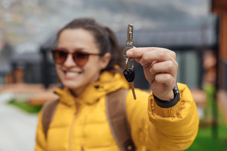 A young woman in a yellow down jacket holds the keys to a vacation home in a mountain areaの写真素材