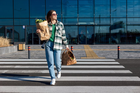 Woman crosswalk the road from a shopping center holding shopping paper bags with a groceries