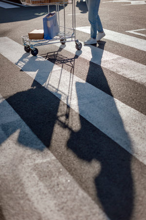 Womans shadow walks with Shopping cart on marked crosswalkの写真素材