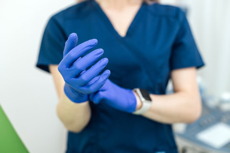 Female doctor puts on white gloves before a patient appointment.の写真素材