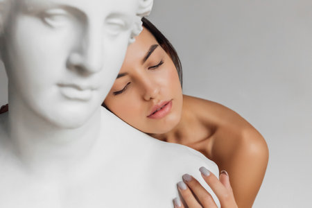 Portrait of young beautiful woman standing near gypsum sculpture Venus faceの写真素材